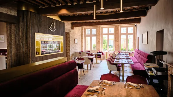 Restaurant avec des tables dressées, des canapés rouges et une vue sur une cour à travers de grandes fenêtres