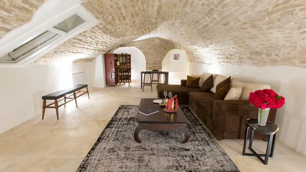 Living room with sofa, coffee table, rug, and flowers in a space with stone walls and a vaulted ceiling with a skylight.