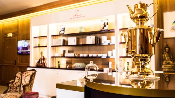 Un samovar en métal poli est posé sur un comptoir dans un intérieur élégant avec des étagères remplies de produits et une chaise décorative à gauche