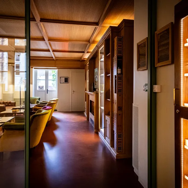 Un couloir avec une porte vitrée menant à une pièce contenant des canapés et des tables, et une étagère remplie de boîtes de cigares