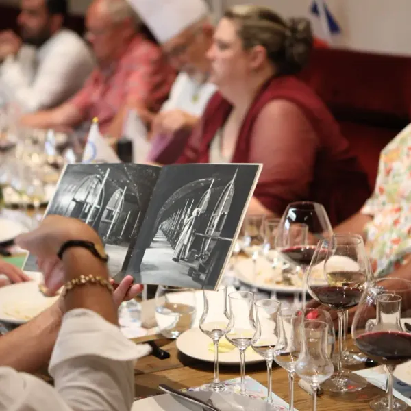 A group of people sitting around a table with wine glasses, examining a black-and-white image.