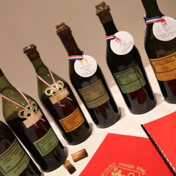 A collection of wine and spirits bottles with commemorative labels of the Olympic Games and medals, arranged on a table.