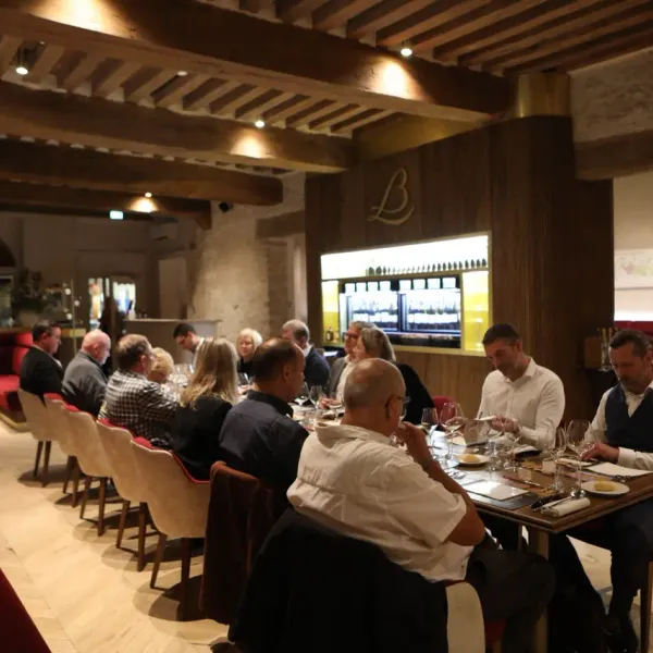 A group of people is sitting around tables in a rustic restaurant, discussing and tasting dishes.