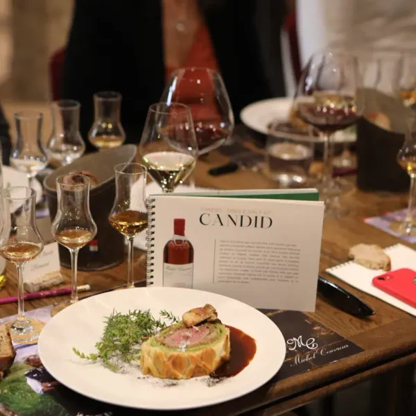 Table set with wine glasses, a bottle, and a plate with a culinary preparation, accompanied by notes and a smartphone.