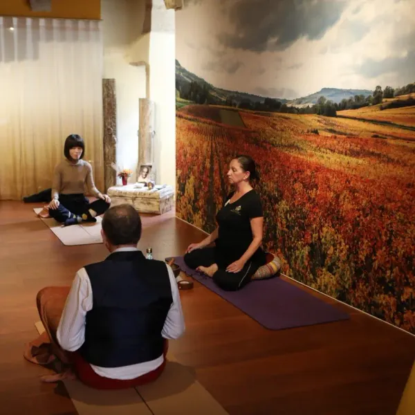 A group of people is practicing meditation in a room with a large wall mural depicting fields.