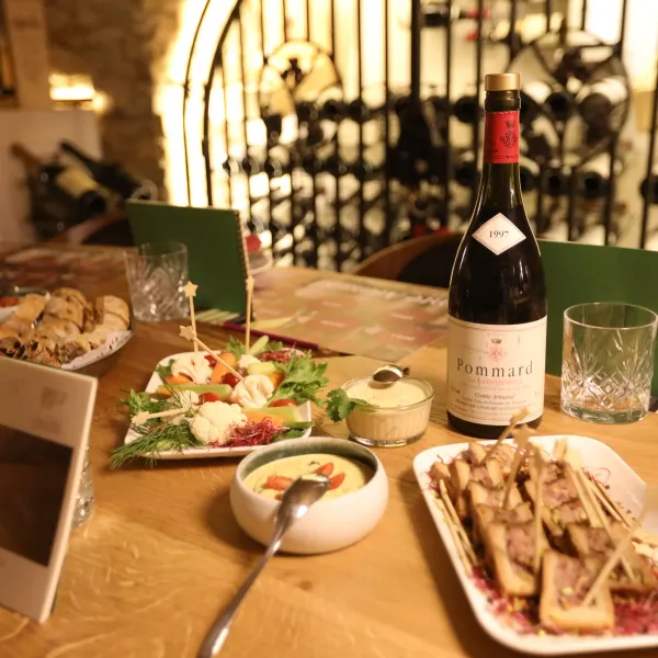 Bottle of Pommard wine on a table with various dishes and glasses in a wine cellar