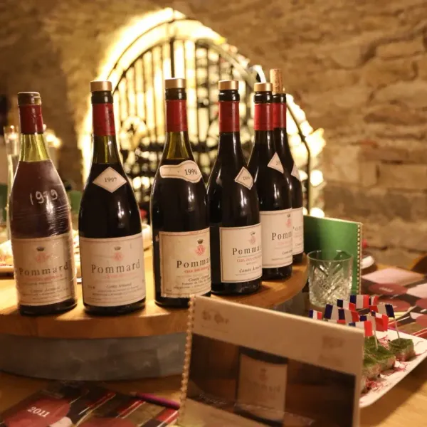 Bottles of Pommard wine from different years arranged on a wooden table with glasses and plates