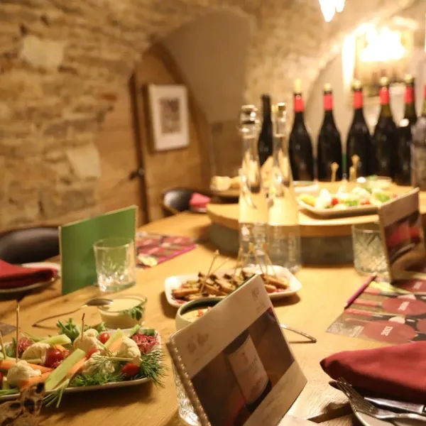 Table set with dishes, wine bottles, and glasses in a rustic setting with stone walls.