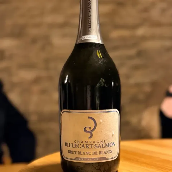 Bottle of Billecart-Salmon Brut Blanc de Blancs Grand Cru placed on a wooden table in front of a stone wall