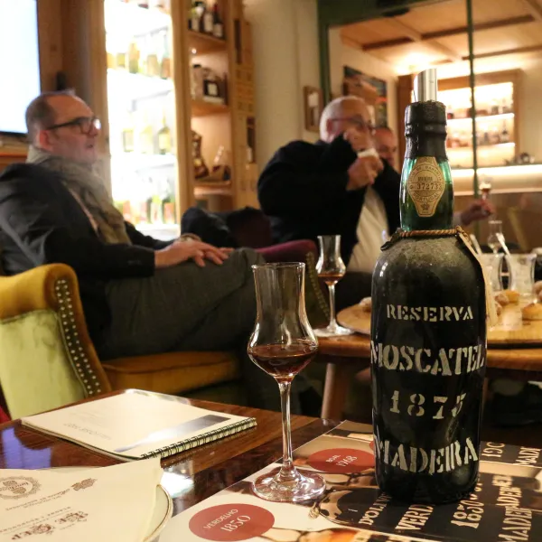 A man sitting in a restaurant with a bottle of wine "Reserva Moscatel 1875" on the table in front of him