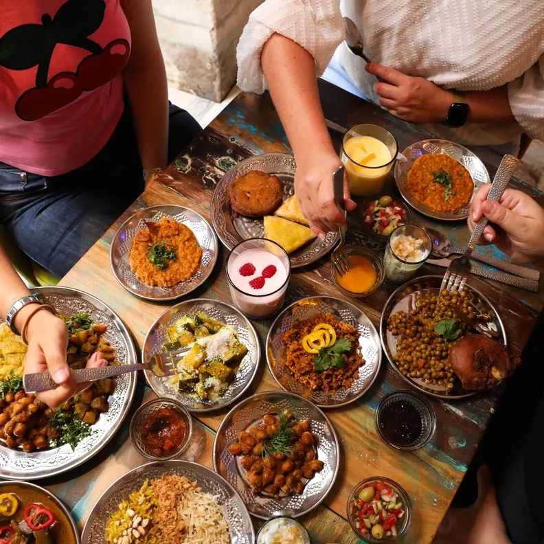 Plusieurs personnes assises autour d'une table partagent un repas composé de nombreux plats traditionnels indiens servis dans des assiettes métalliques