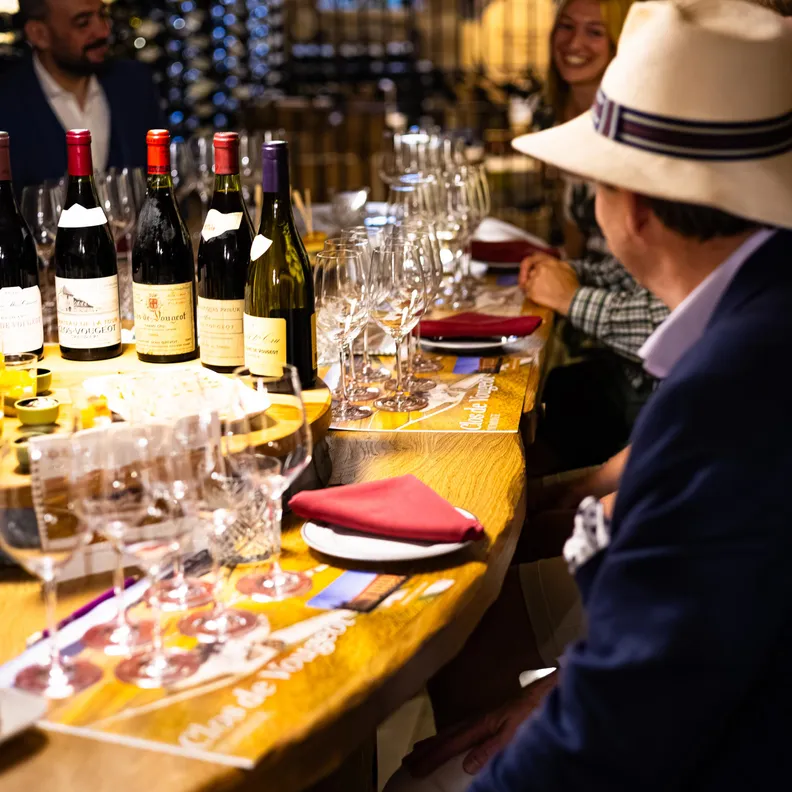 Plusieurs bouteilles de vin et verres à vin sur un comptoir en bois avec des personnes autour