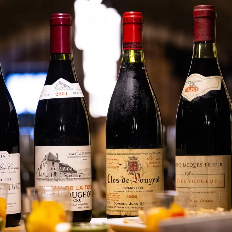 Plusieurs bouteilles de vin avec des étiquettes détaillées sont alignées sur une table décorée de fleurs