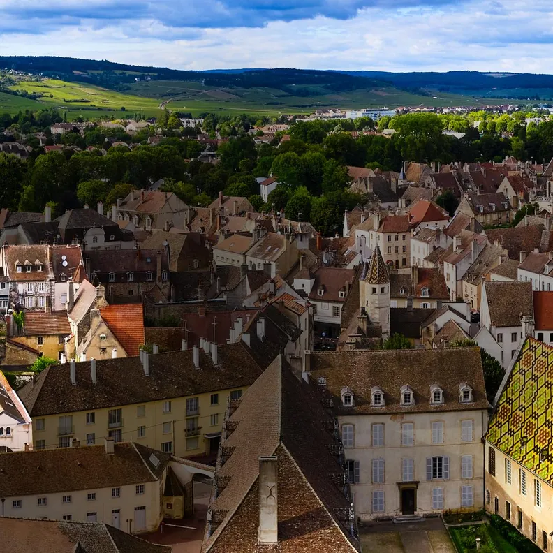 Historic town with tiled roofs and traditional architecture, seen from a high point, surrounded by lush green hills