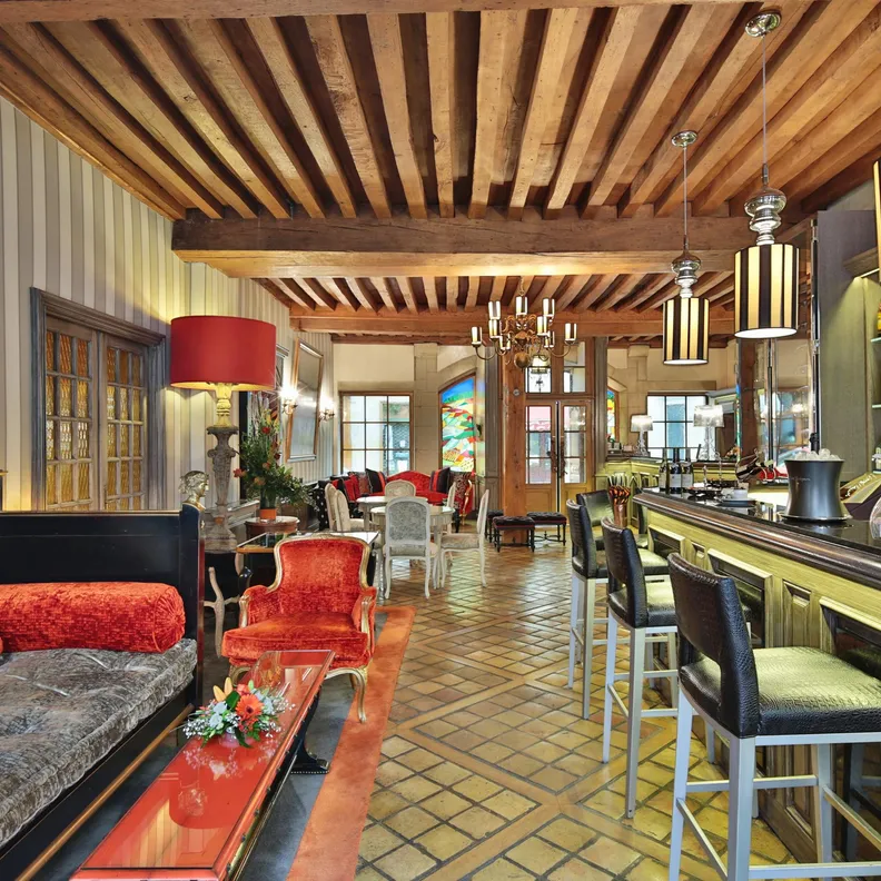 Elegant bar with counter, stools, sofas, and chairs, decorated with mirrors, lighting, and alcohol bottles on shelves.