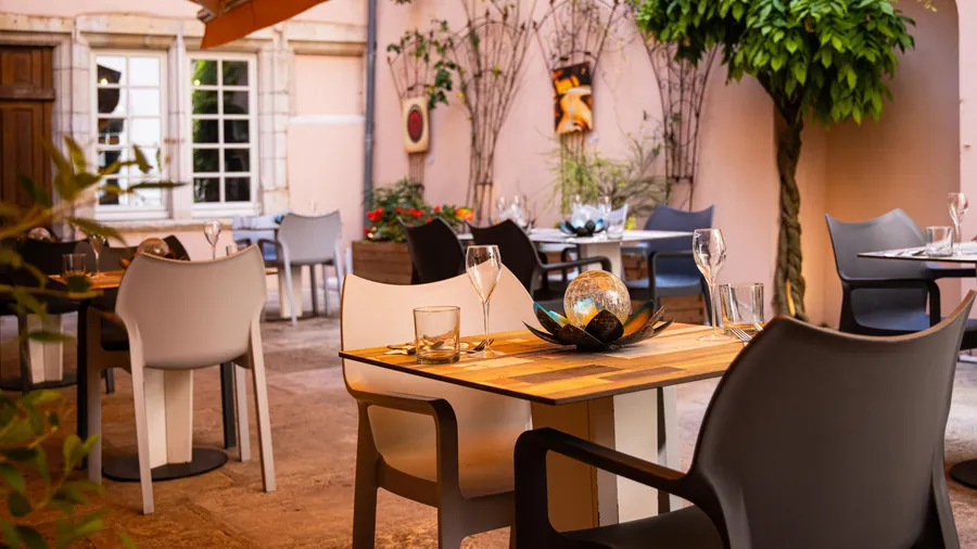 Une terrasse de restaurant avec des tables en bois, des chaises modernes et des verres à vin, entourée de plantes et de murs décorés