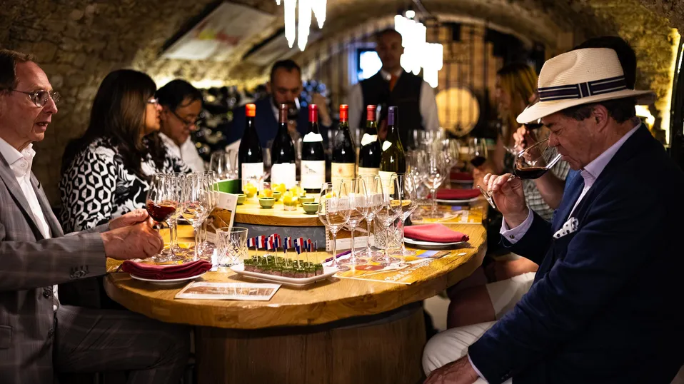 Un groupe de personnes déguste du vin autour d'une table garnie de verres et de bouteilles dans un cadre souterrain