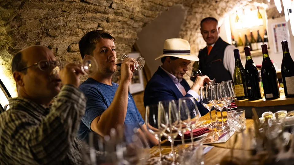 Un groupe de personnes déguste du vin dans un caveau avec des bouteilles et des verres sur une table