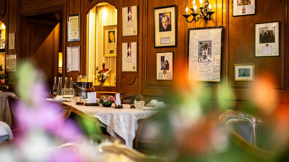 Intérieur d'un salon avec des murs en bois ornés de cadres, de photos et de diplômes, une table dressée avec des verres et des fleurs